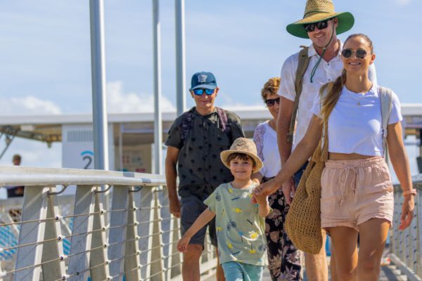 A young boy holding his mothers hand as he walk on a Hopo wharf