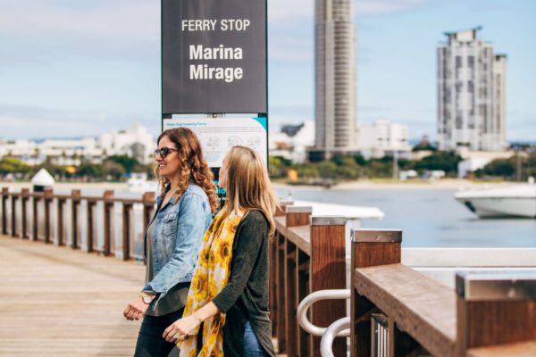 Two young woman walking on ferry whatf with Marina Mirage sign behind them.